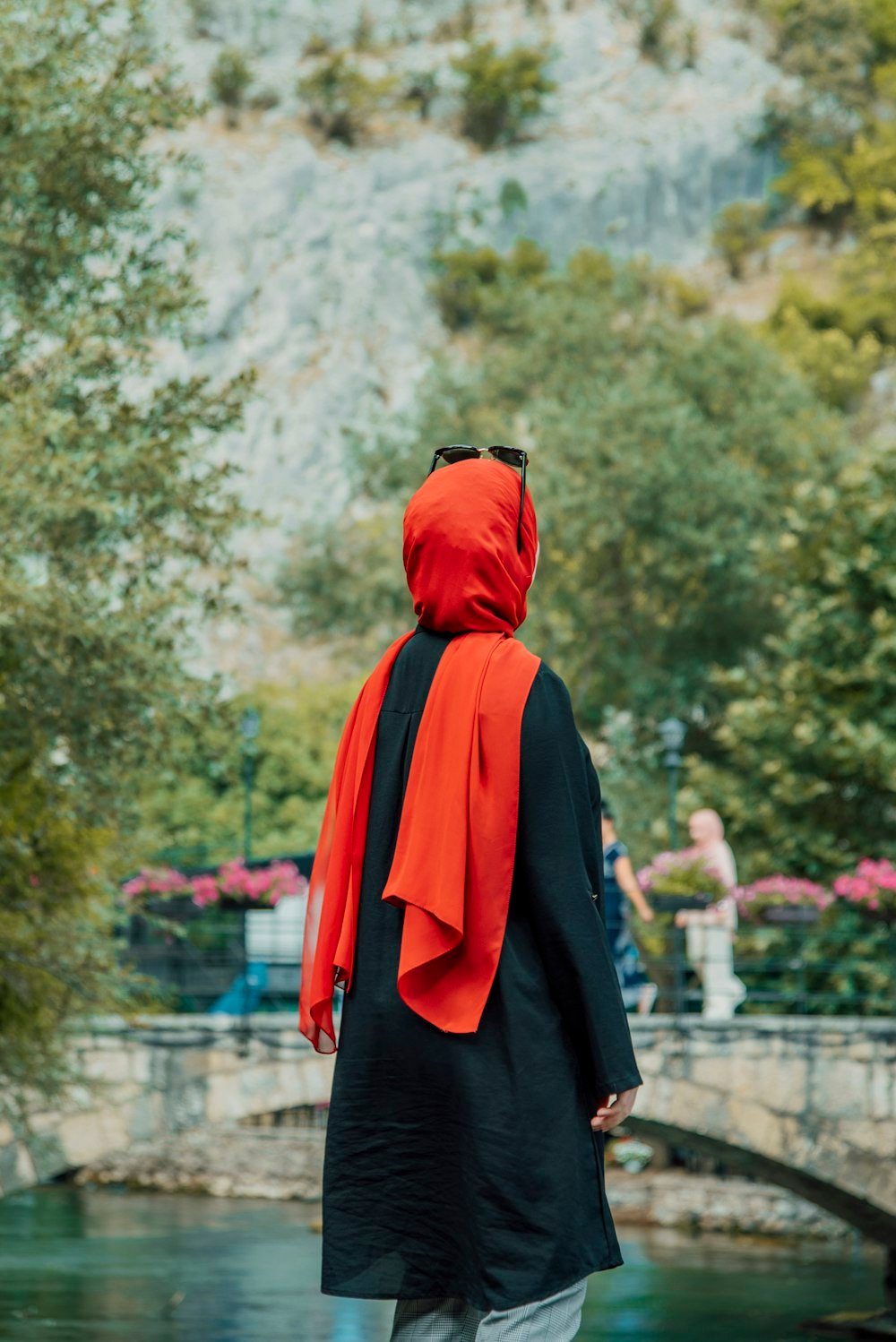 A woman in a red hijab seen from behind, standing in a flower garden